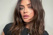 Lucy Hale wearing brunette medium-length hair with some lowlights, chin bangs and waves plus middle part