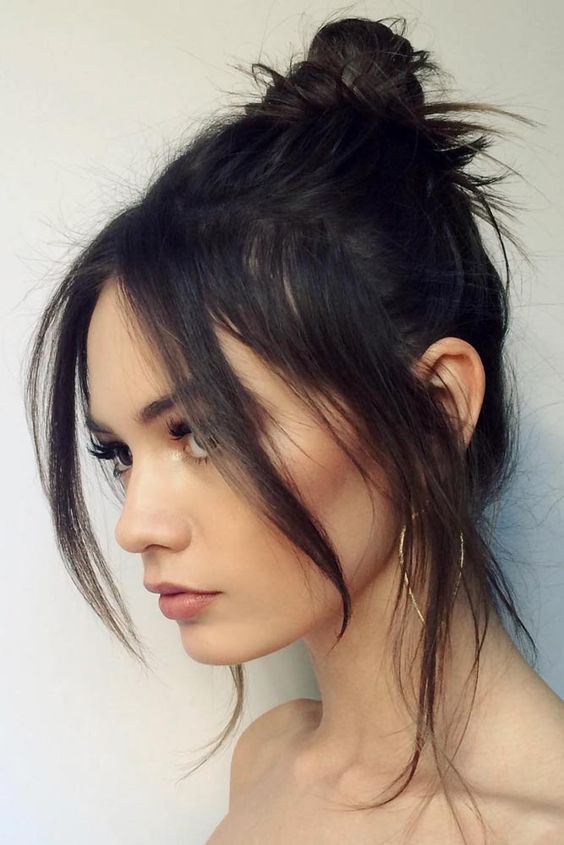 a black messy top knot with chin bangs and some locks down is a chic idea that looks feminine