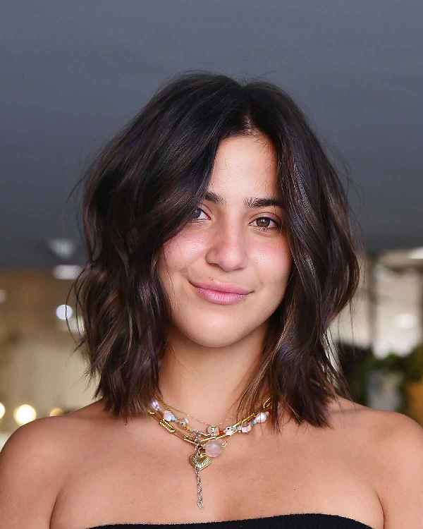 a dark brown layered lob on thick hair, with central part and highlights that give texture to the look