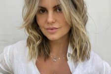a long layered bob with blonde balayage, a darker root, face-framing bangs and waves and texture is messy and cool
