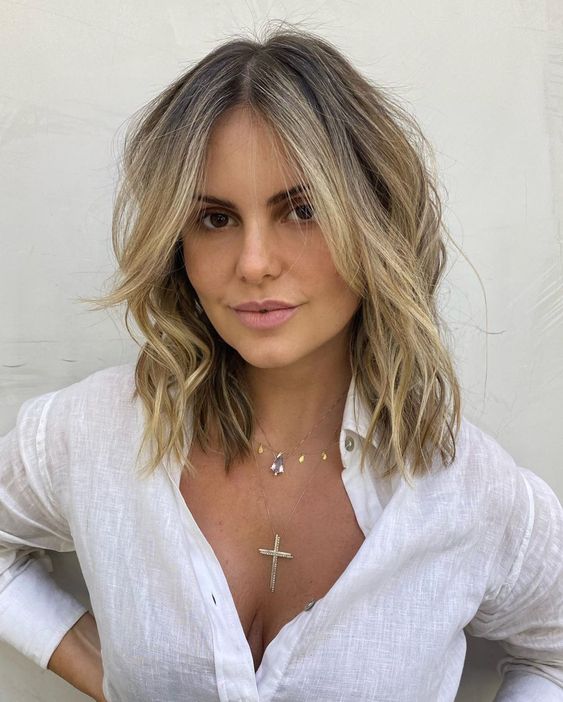 a long layered bob with blonde balayage, a darker root, face-framing bangs and waves and texture is messy and cool