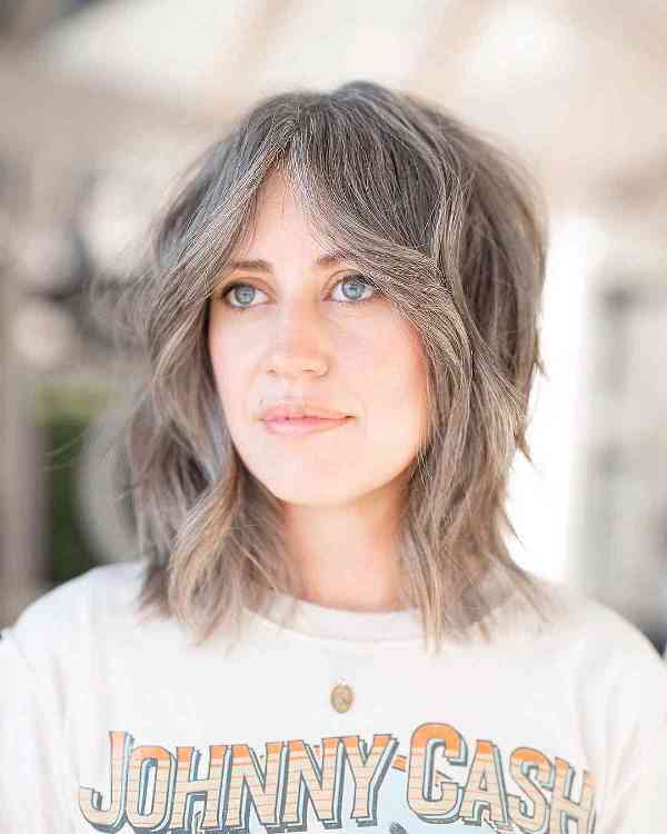 a messy layered long bob haircut with curtain bangs and textured layers and a greyish color that works perfect with blue eyes