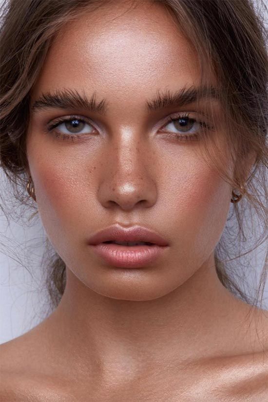 a summer bronze-inspried makeup with a pink glitter lip, blush and a lot of highlighter, fluffy eyebrows and accented skin