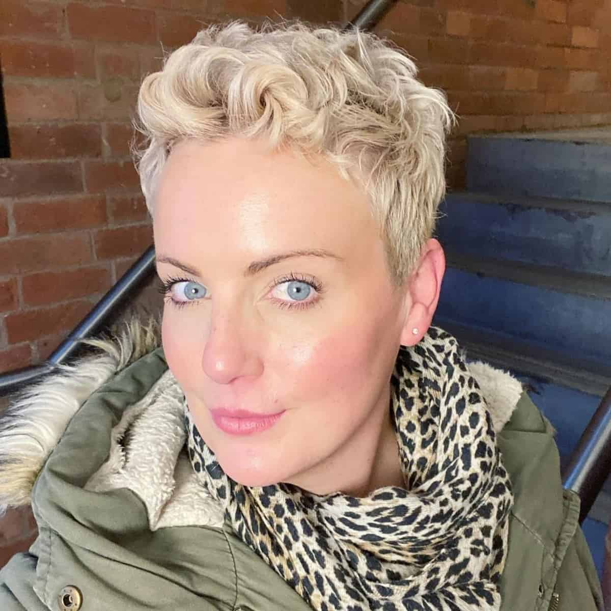 a super short blonde wavy pixie haircut with some extra length on the sides and back and it looks chic