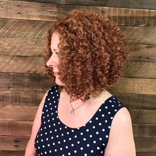 an asymmetrical curly bob in a soft brownish ginger shade is a cool idea for anyone, it looks cool and fresh