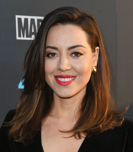 Aubrey Plaza wearing a medium layered haircut, with side parting and face-framing layers looks chic