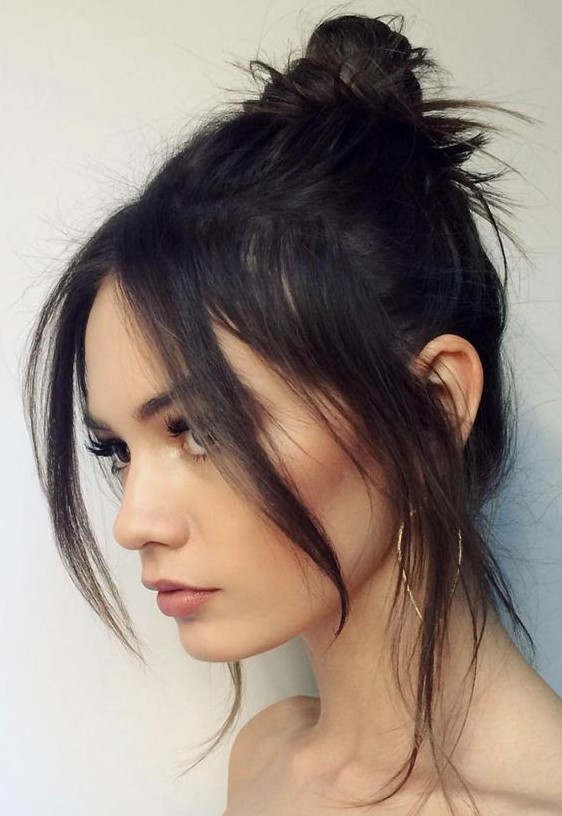 a black messy top knot with face-framing layers and some locks down is a chic idea that looks feminine