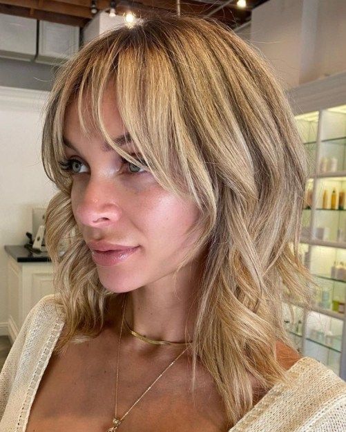 a blonde medium length choppy layered haircut with side and wispy bangs paired looks cool, fresh and very modern