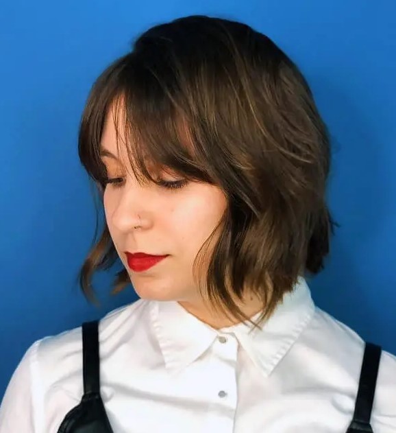 a dark brunette shaggy bob with Bardot bangs and a bit of highlights is a stylish and catchy idea