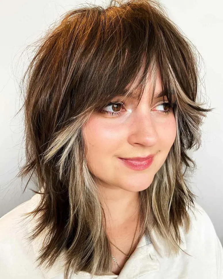 a layered shaggy haircut with blonde highlights and curtain bangs looks cool on thick hair and brings a 70s vibe to the look