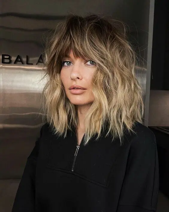 a lovely and dimensional outgrown bob haircut with a darker root, blonde balayage and a fringe is wow