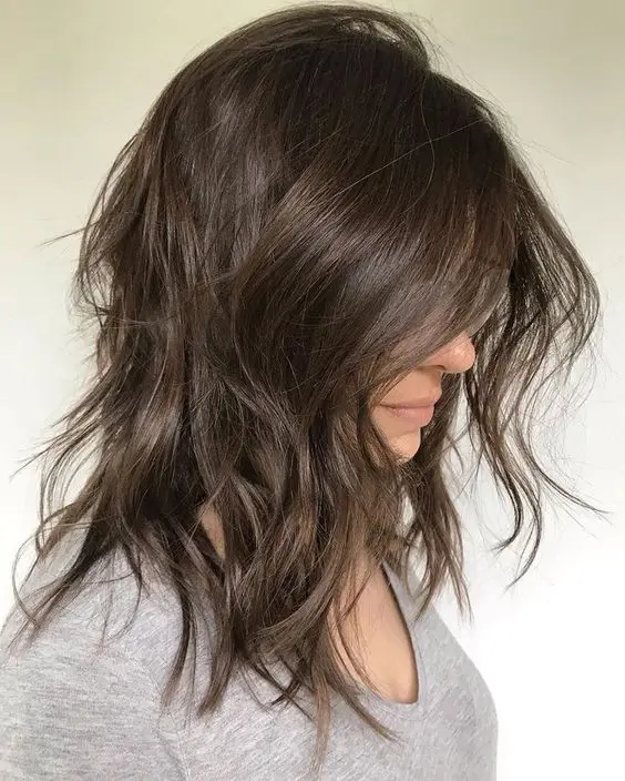 a messy dark brown medium-length choppy haircut with shaggy layers and a bit of wavy ends