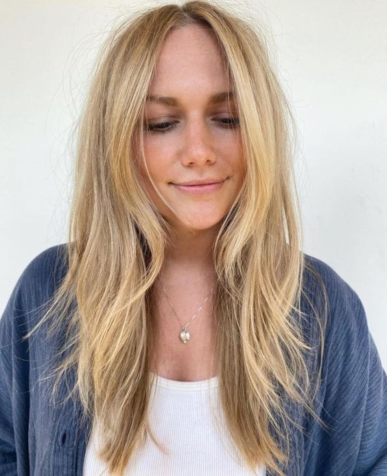 Long and messy blonde hair with layers including face framing ones, with central part and texture is cool