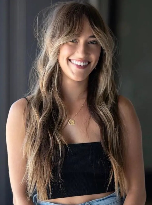 long brunette wavy hair with blonde highlights and Bardot curtain bangs plus a lot of texture and a bit of mess