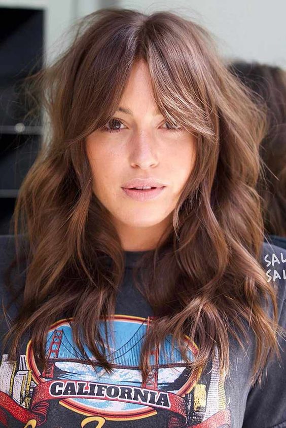 Long wavy brown hair cut in layers and with a Bardot fringe is a lovely idea that feels a bit rock style