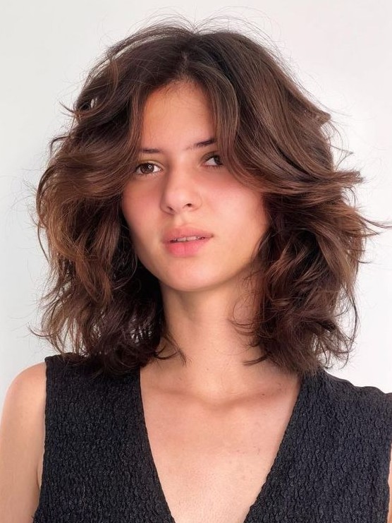 A beautiful dark brunette medium length butterfly haircut on wavy hair, with a lot of dimension