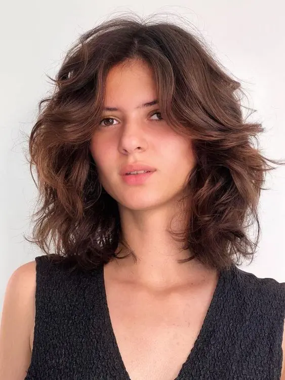 a beautiful dark brunette medium length butterfly haircut on wavy hair, with a lot of dimension