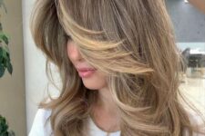 a beautiful medium butterfly haircut in bronde, with londe highlights, with curved locks and side bangs is a cool idea
