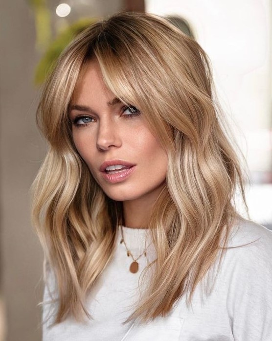 A beautiful medium length hairstyle with waves, a darker root and soft wavy curtain bangs that accent the face