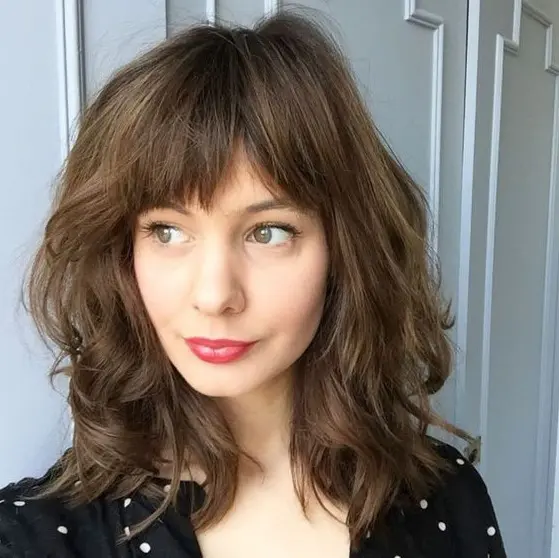 a beautiful medium length wavy haircut with bottleneck bangs is a chic and girlish idea inspired by Parisians
