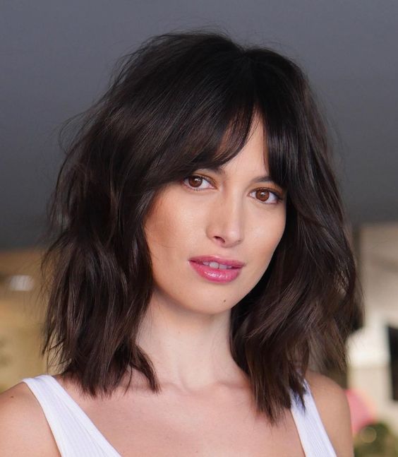 a black dimensional medium-length hairstyle with slight waves and bottleneck bangs is a chic and sexy idea