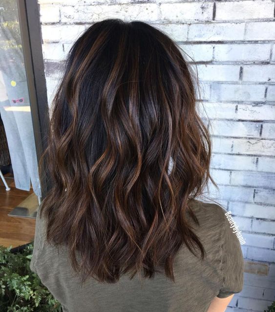 A black medium length wavy hairstyle with caramel highlights and waves is a timeless idea to rock
