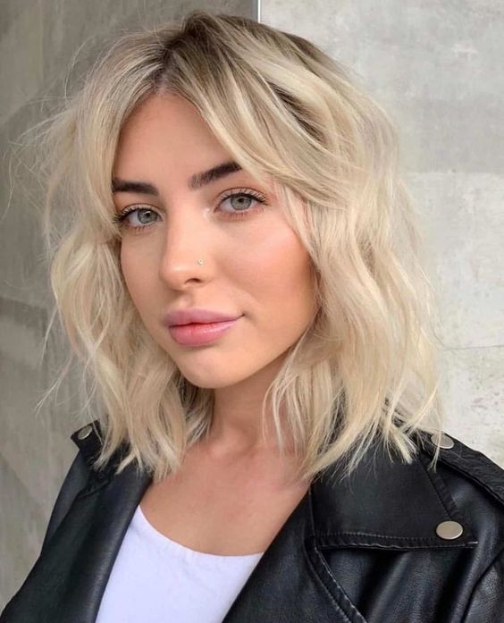 A bleached blonde shoulder length hairstyle with messy and wavy volume with a dark root is a lovely idea