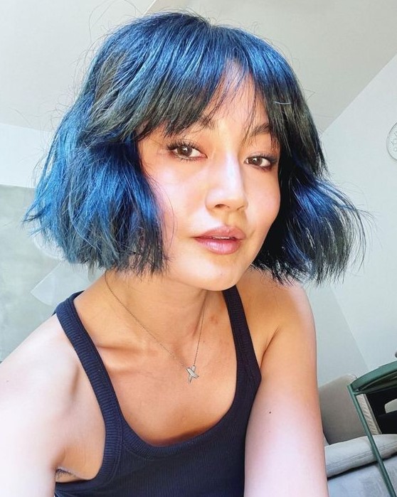 a bold black blue messy and textured bob with wispy and bottleneck bangs plus some waves is a catchy and chic idea