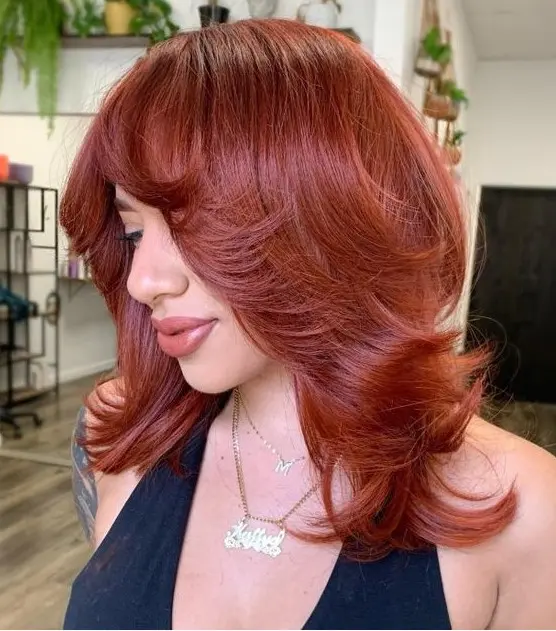 a bold red medium butterfly haircut with curled ends and a lot of volume looks very eye-catchy and very bright