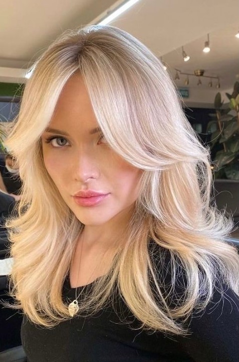 a bright blonde butterfly haircut with wavy ends and a bit of volume, with curtain bangs, is a stunning solution to rock