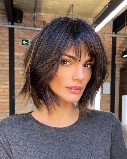 a dark, almost black asymmetrical shaggy bob with highlights and wispy bangs that accent that relaxed and messy look