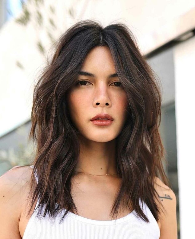 A dark brown middle parted textured lob with caramel balayage and slight waves plus a lot of volume is a gorgeous idea