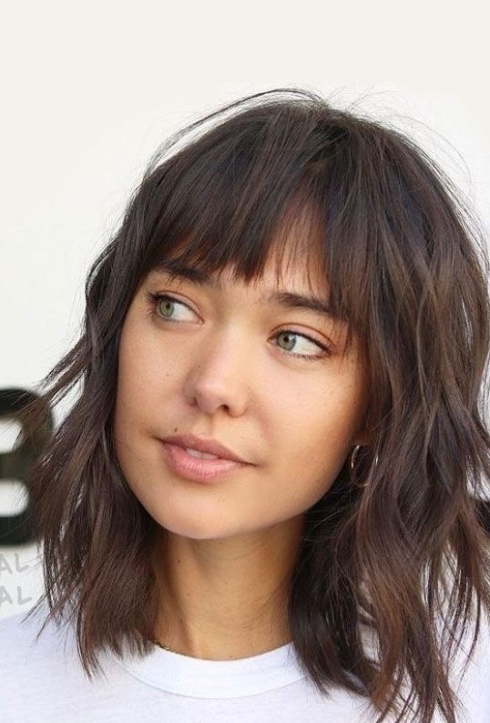 a dark brunette wavy medium-length hairstyle with shaggy layers and wispy bangs is a lovely and relaxed idea to try for summer