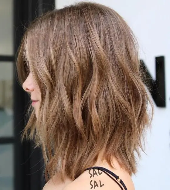 A delicate and soft brown choppy long bob with subtle highlights and waves and face framing layers is cool