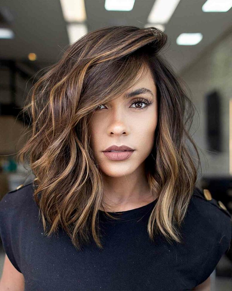 a dimensional asymmetrical medium-length haircut with side bangs and caramel highlights that bring even more dimension