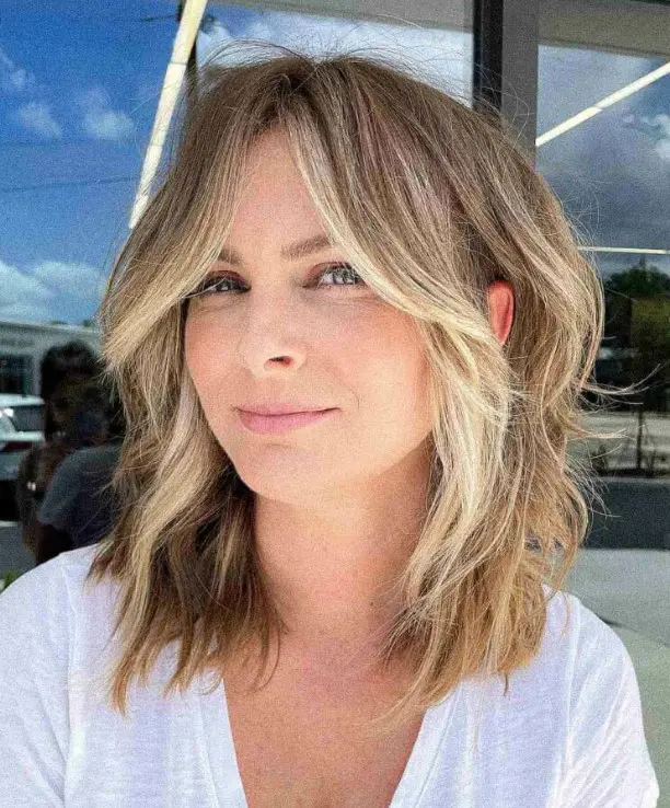 A flattering face framing wavy lob with curtain bangs and blonde highlights and money piece is a fresh and cool idea