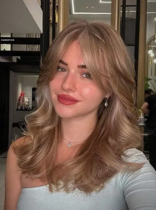 a gorgeous bronde wavy hairstyle done on a butterfly haircut, with curtain bangs, is adorable and very chic