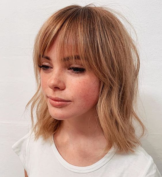 a ligth ginger long bob with messy waves and wispy bangs is a chic and refreshing idea, it catches an eye with its color