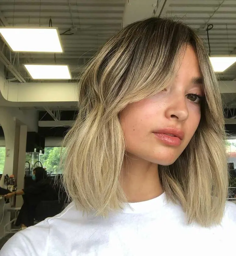 a long bob with blonde balayage and a darker root plus curtian bangs for a shaggy and effortless look