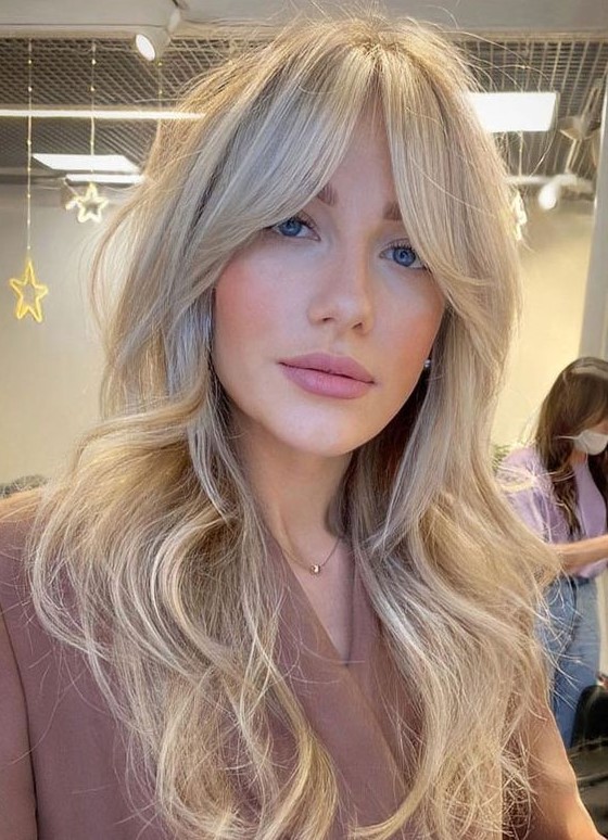 a long creamy blonde wavy hairstyle with curtain bangs is a chic and feminine idea to try right now