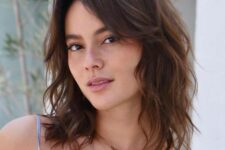 a lovely brown medium-length hairstyle with caramel balayage, waves and curtain bangs to frame the face