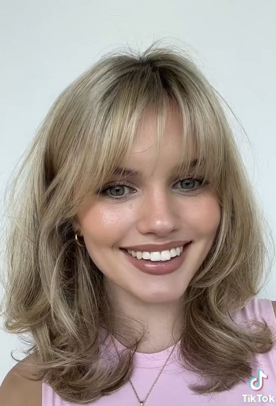 a medium blonde butterfly haircut with wispy bangs and waves is a pretty idea and it feels like the 90s