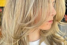 a medium-length blonde butterfly haircut with curled ends, a bit of volume and a darker root is a stylish idea