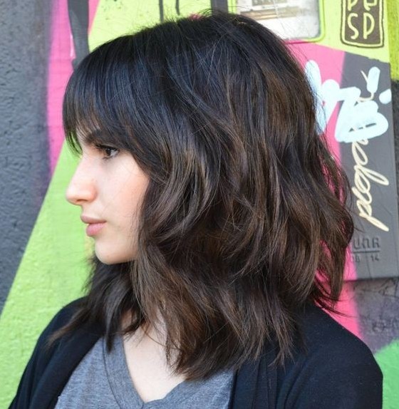 a medium length haircut with bangs, waves and much dimension is a modern option