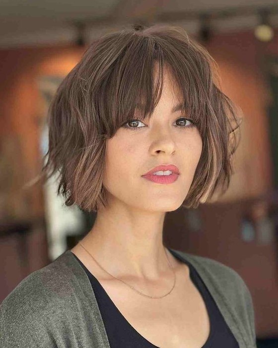 a pretty and messy brown chin length bob with a bit of waves and bottleneck bangs plus highlights is amazing