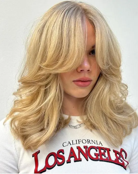 a stunning blonde butterfly haircut with curtain bangs and wavy ends plus a lot of volume is amazing and chic