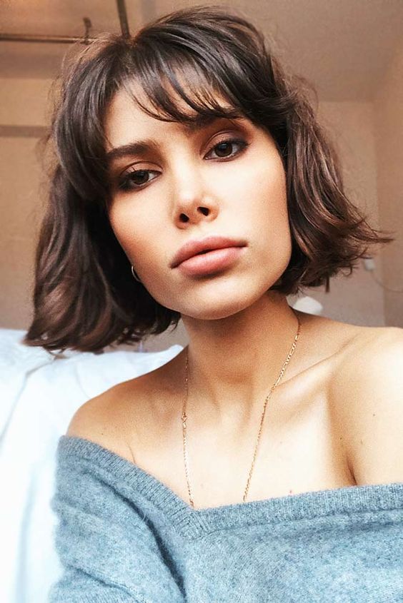 a stylish dark burnette chin-length bob with wispy bangs and messy waves is a cool idea to rock right now