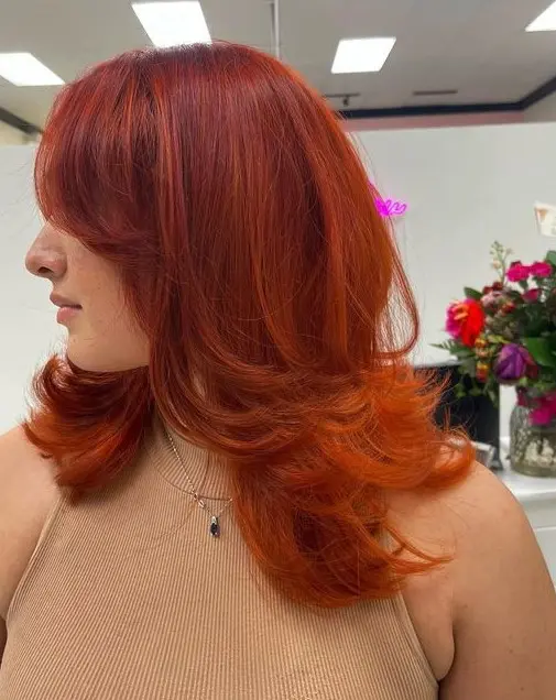 a super bright red and orange butterfly haircut on medium hair, with curtain bangs and curled ends is wow