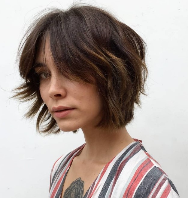 A textured brown chin length bob with a bit of caramel balayage and a lot of texture looks cool