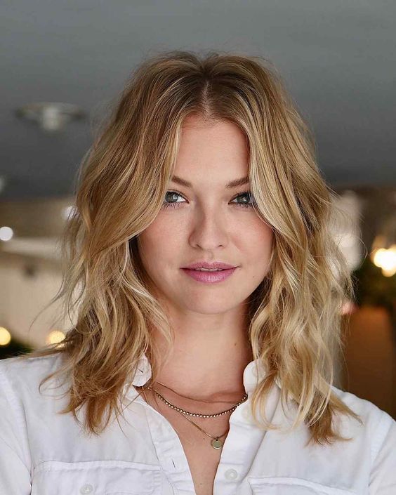 a wavy blonde shoulder-length haircut with a darker root, side bangs to frame the face looks effortless and cool